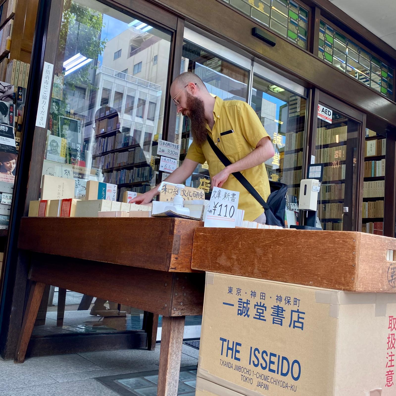 A photo of a man with a long beard looking through used books outside a store in Tokyo.